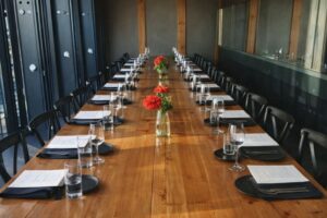 Långt dukat bord för privat middag med menyer, glas och röda blommor.